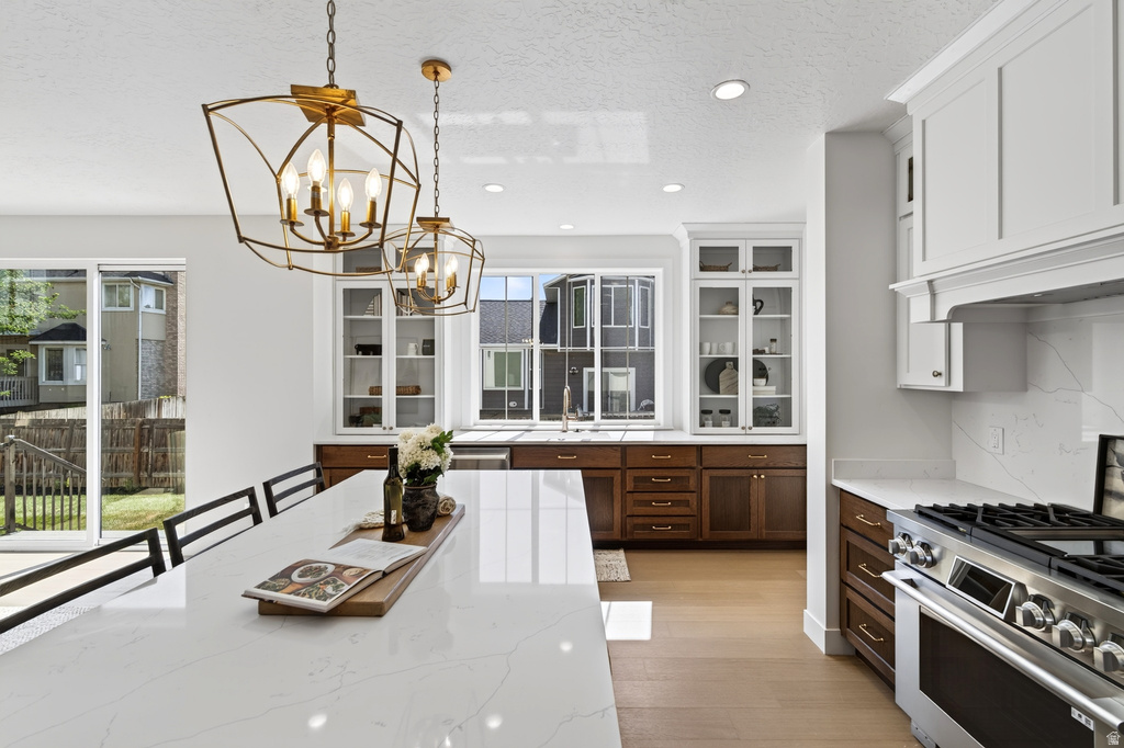 Kitchen featuring a large central island with a light-toned countertop, dual gold-finish pendant lights, light wood-finish flooring, white upper cabinetry, and dark wood-finish lower cabinetry