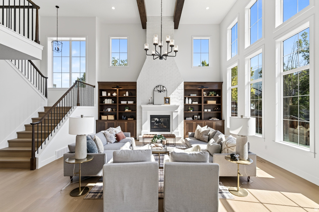 Two-story living area featuring a white brick fireplace, built-in dark wood shelving, wood-finish flooring, and a grand staircase with wrought iron balusters