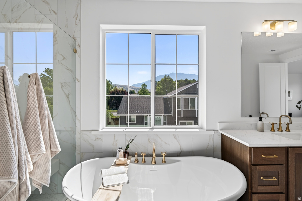 Freestanding soaking tub with brushed gold fixtures, set against a window with mountain scenery