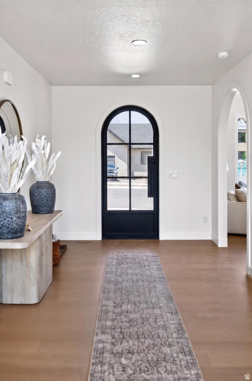 Arched entry door with black grid-pane glass and hardware, recessed ceiling lighting, wood-finish flooring, and white baseboards