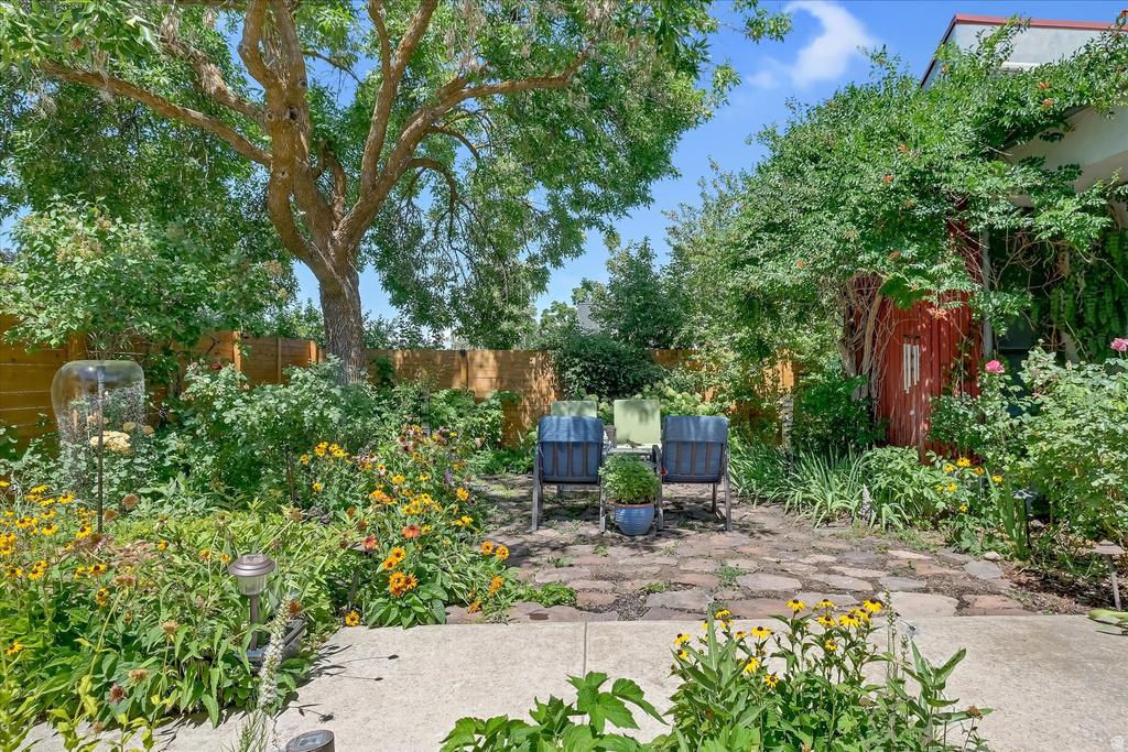 Mature trees shade an expansive backyard featuring a stone patio and vibrant garden beds