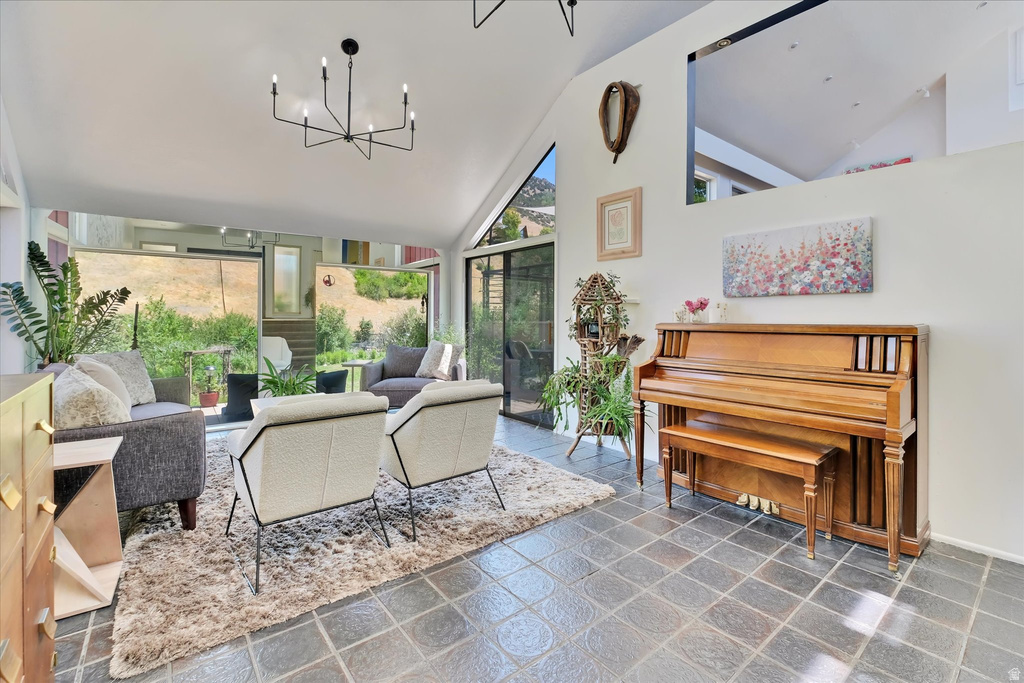 Spacious living area featuring a vaulted ceiling with a contemporary chandelier, large windows, slate tile flooring, and white walls