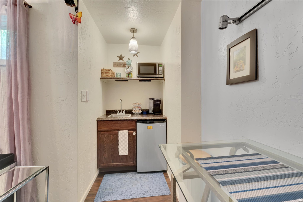 Compact kitchen area featuring a built-in microwave, under-counter refrigerator, sink with faucet, wood-finish cabinetry, and overhead shelving
