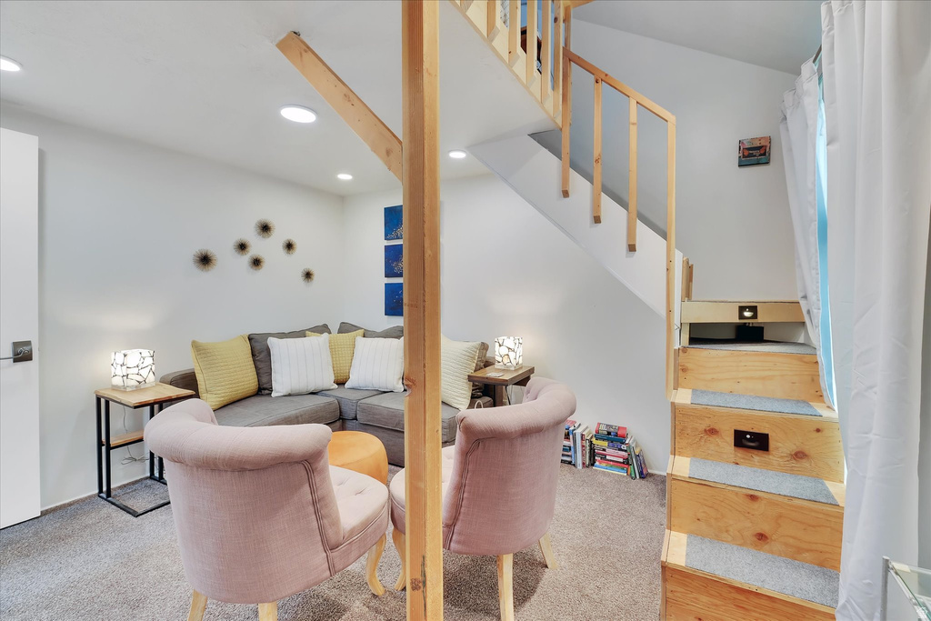 Carpeted living area featuring recessed lighting, a built-in wooden staircase with integrated lighting, and a white interior door with dark hardware