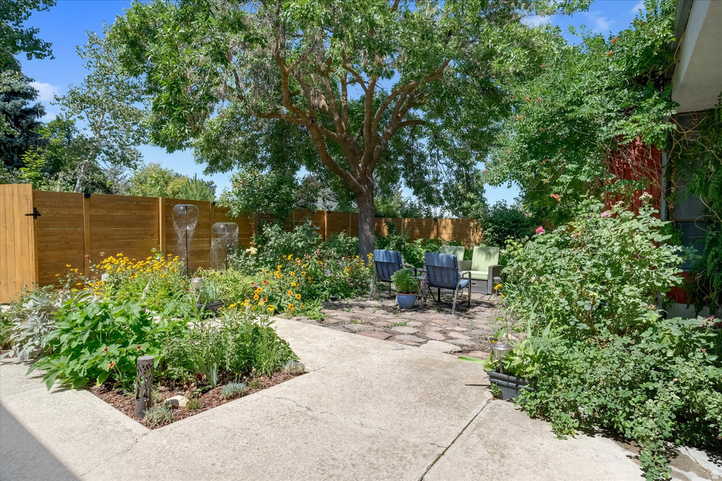 Landscaped backyard featuring a mature tree, stone patio, and perimeter fencing