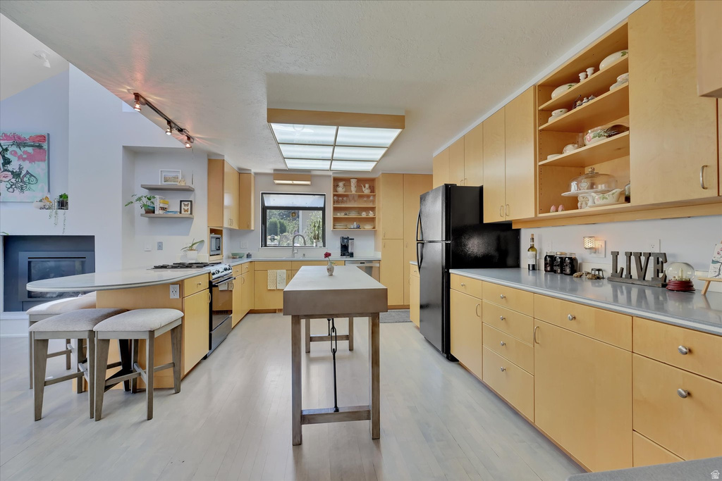 Expansive kitchen featuring light wood-finish cabinetry, black appliances, light-toned countertops, and a skylight