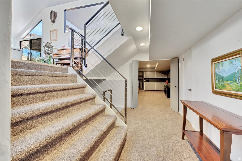 Carpeted staircase featuring a modern cable railing system and recessed lighting