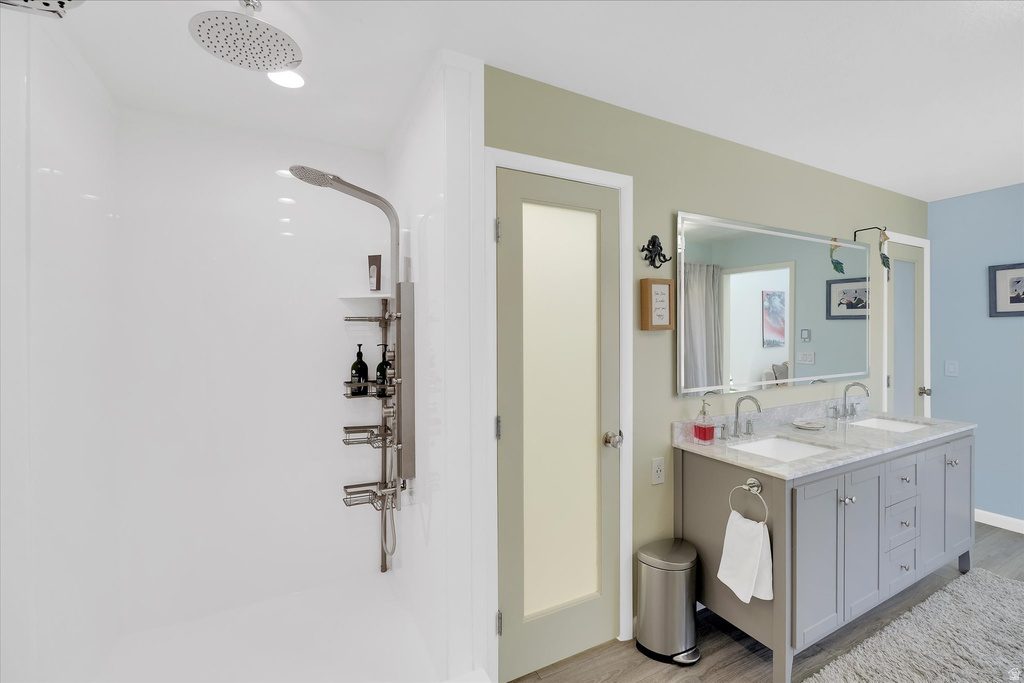 Bathroom featuring a dual vanity with undermount sinks and a stone countertop, a large framed mirror, and a walk-in shower with a rain shower head and a multi-function shower panel