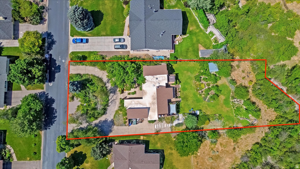 Aerial view of a sprawling property featuring a main residence with a brown roof and light-colored siding, a paved circular driveway, established landscaping, and a large undeveloped natural area