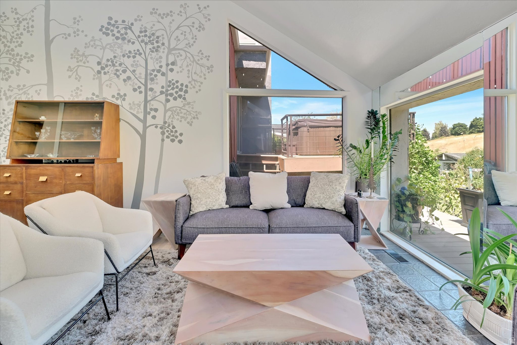 Expansive windows and sliding glass doors illuminate a contemporary living area featuring a decorative wall mural, tiled flooring, and a terraced outdoor area with a spa