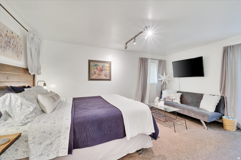 Bedroom featuring a wood-finish headboard, wall-mounted track lighting, and soft carpet flooring