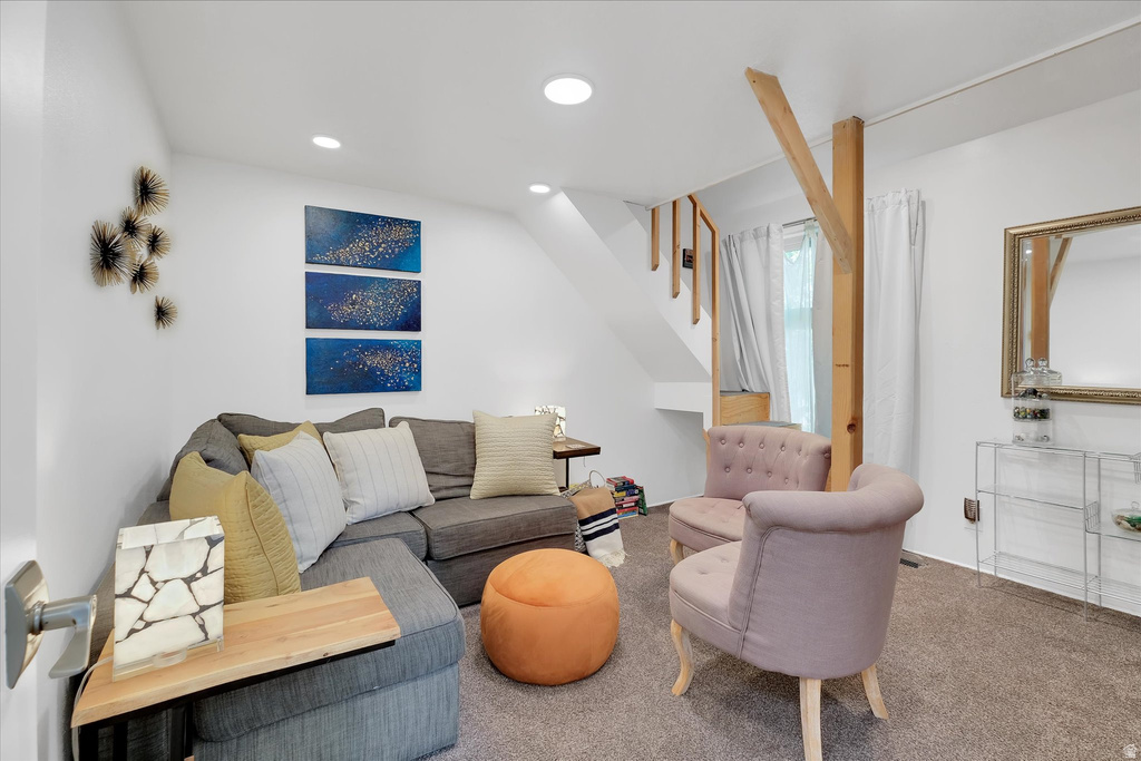 Carpeted living space featuring recessed lighting, white walls, and an exposed wooden support beam