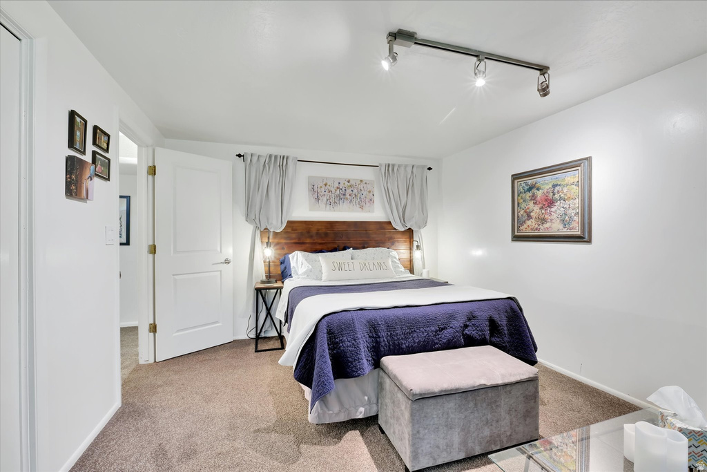 Carpeted bedroom with a built-in wood headboard, white walls, and track lighting