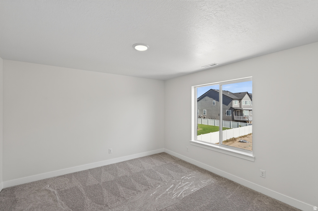 Spacious room featuring neutral carpeting, a large window, white baseboards, and a recessed ceiling light