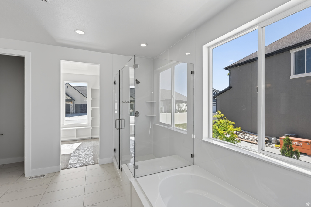Bright bathroom featuring a large soaking tub, glass-enclosed shower, tile flooring, recessed lighting, and a spacious window