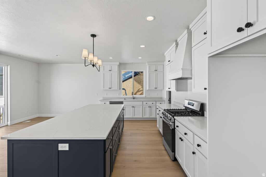 Spacious kitchen featuring an expansive island with a contrasting dark base, light-toned countertops, white cabinetry with dark hardware, stainless steel appliances, and wood-finish flooring