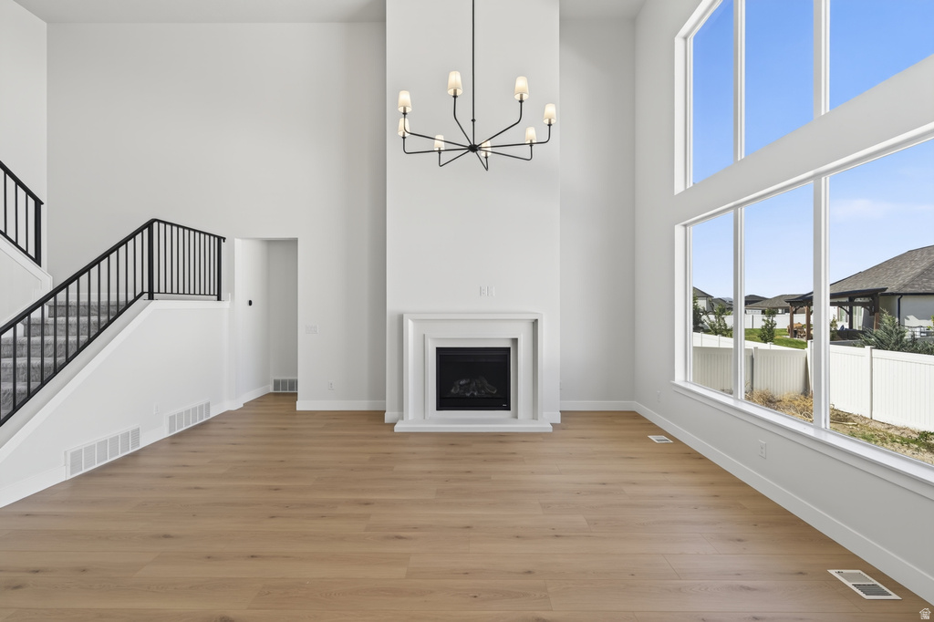 Two-story living area featuring a prominent fireplace with white mantel, oversized windows, wood-finish flooring, and a modern chandelier