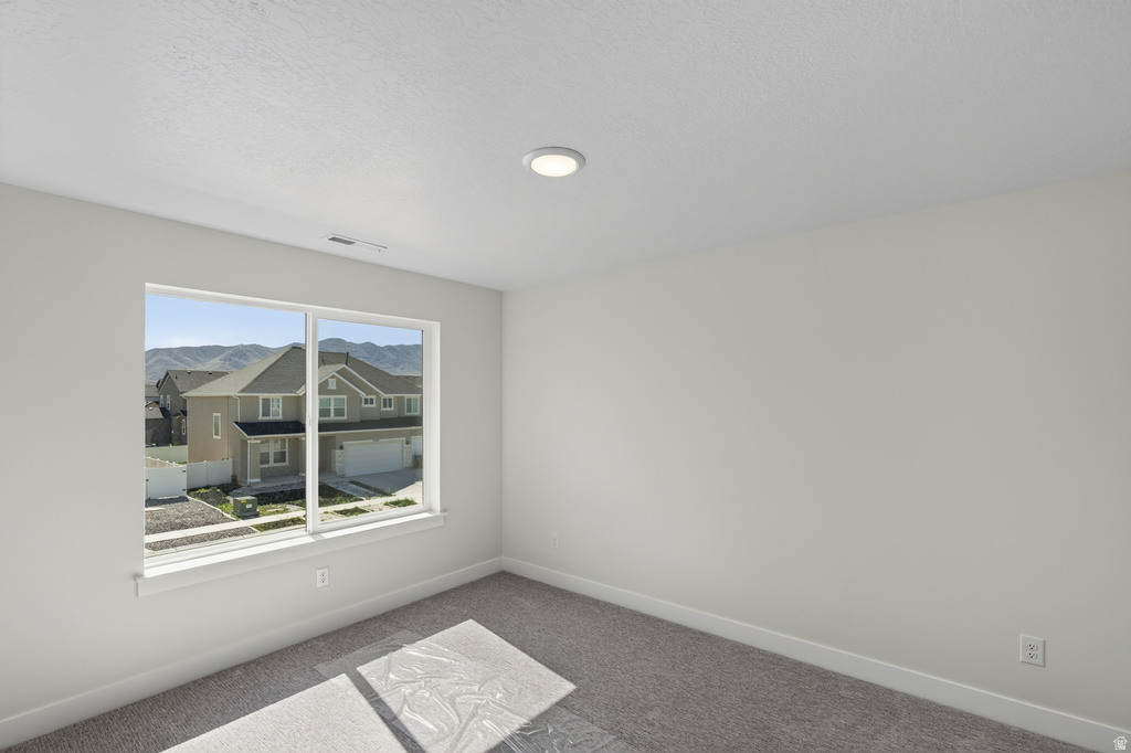 Bright room with a large window, recessed ceiling lighting, textured white walls, and gray carpet flooring