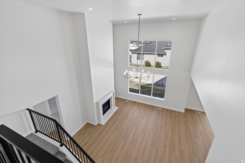 Two-story living area featuring a prominent fireplace with a white surround, wood-finish flooring, and a contemporary black chandelier
