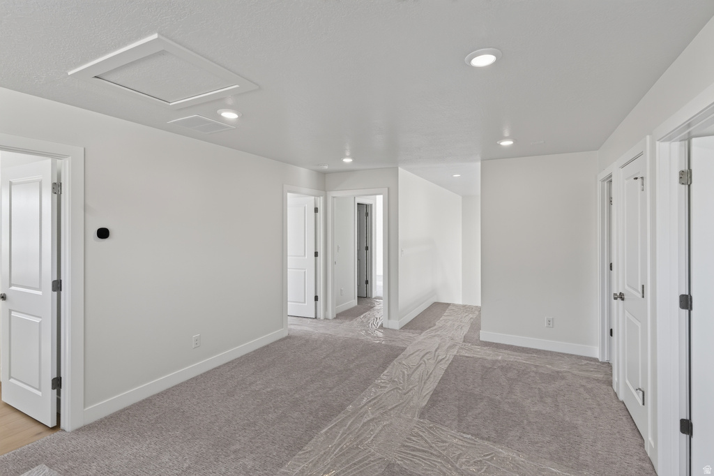 Spacious room featuring light gray carpeting, recessed ceiling lighting, a white wall thermostat, and multiple interior doors with modern hardware