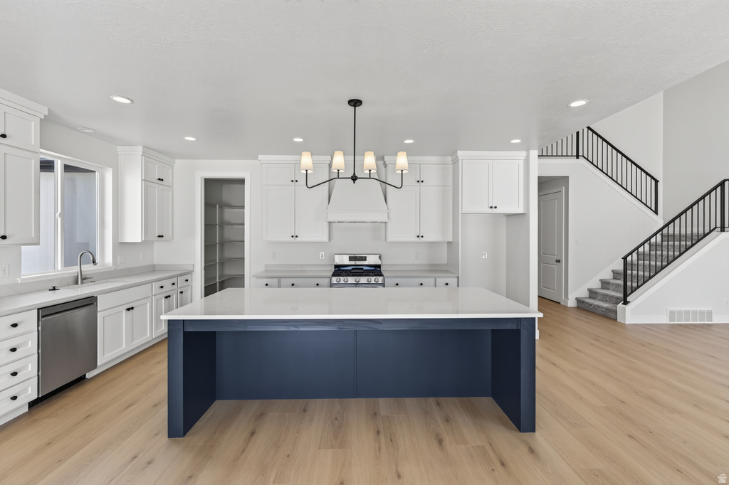 Kitchen featuring a contrasting navy island with a light countertop, white shaker cabinetry, stainless steel appliances, and wood-finish flooring