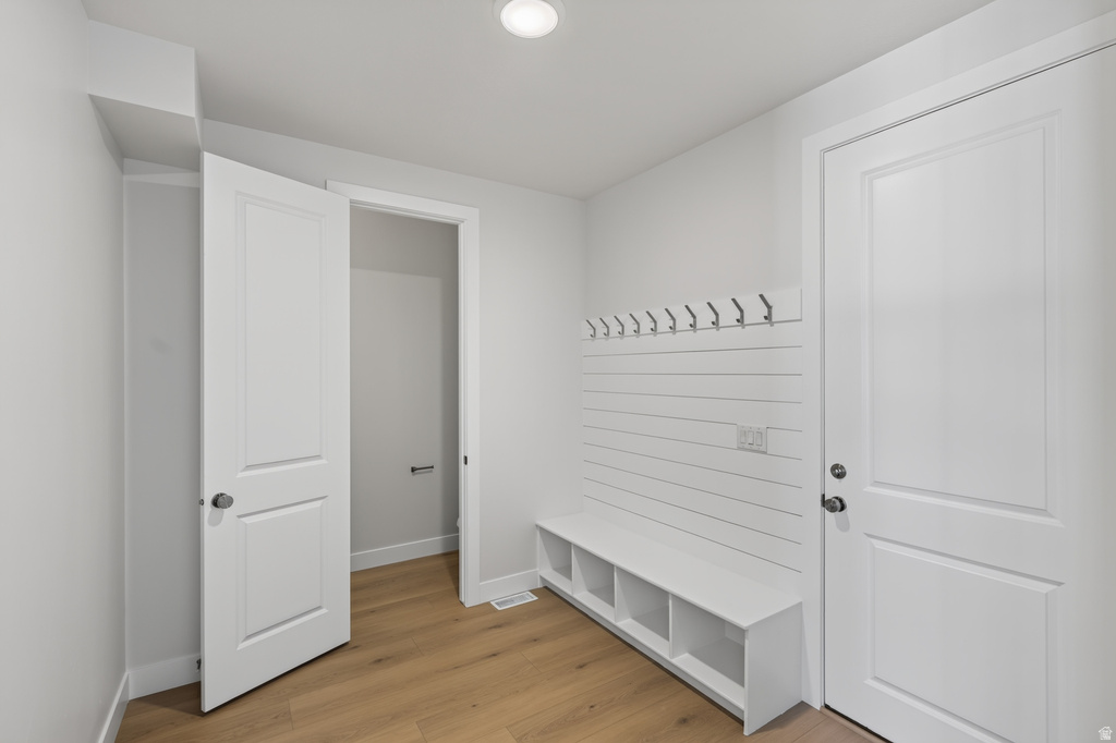 Dedicated mudroom area featuring a built-in bench with cubby storage, wall-mounted coat hooks, and durable wood-finish flooring