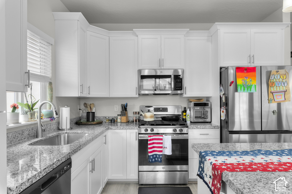 Kitchen featuring white shaker-style cabinetry, stainless steel appliances, speckled stone countertops, and a stainless steel sink with a gooseneck faucet