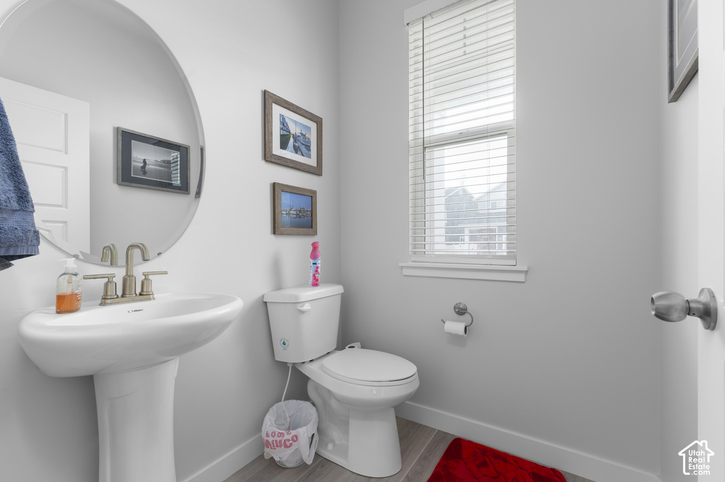 Pedestal sink with brushed nickel faucet, round wall-mounted mirror, and light gray wood-finish flooring