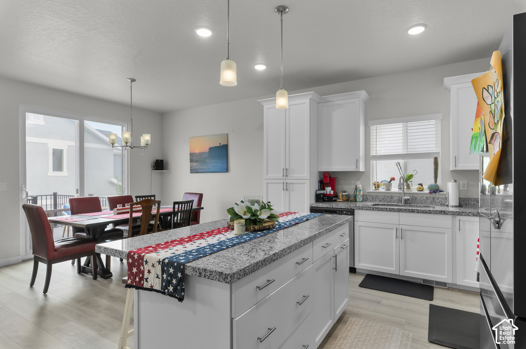 Open-concept kitchen and dining area featuring a central island with a granite countertop, white cabinetry, stainless steel appliances, and wood-finish flooring