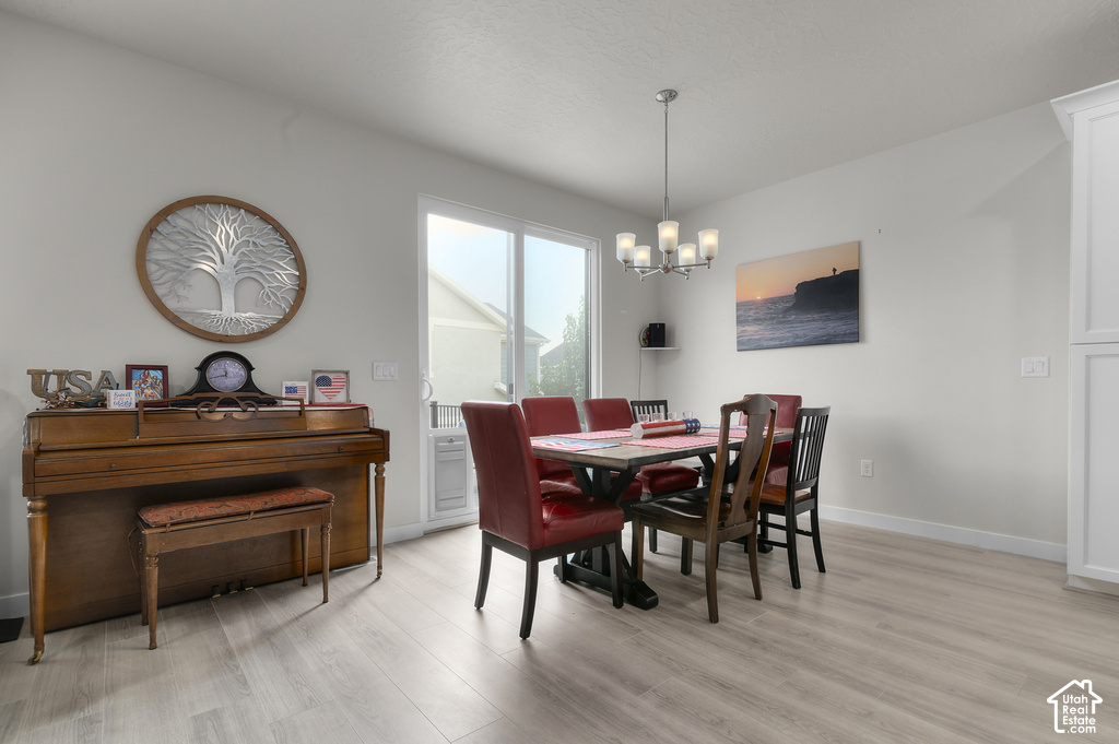 Open-concept space featuring light wood-finish flooring, a contemporary chandelier, white wall paneling, and a sliding glass door providing exterior access