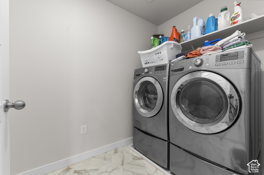 Dedicated laundry area featuring front-loading washer and dryer units, a wall-mounted storage shelf, and light-toned tile flooring