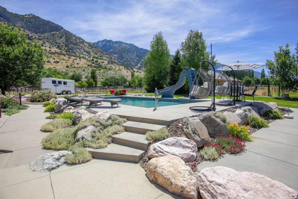 In-ground swimming pool featuring a water slide, concrete pool deck, and a surrounding rock garden with integrated steps