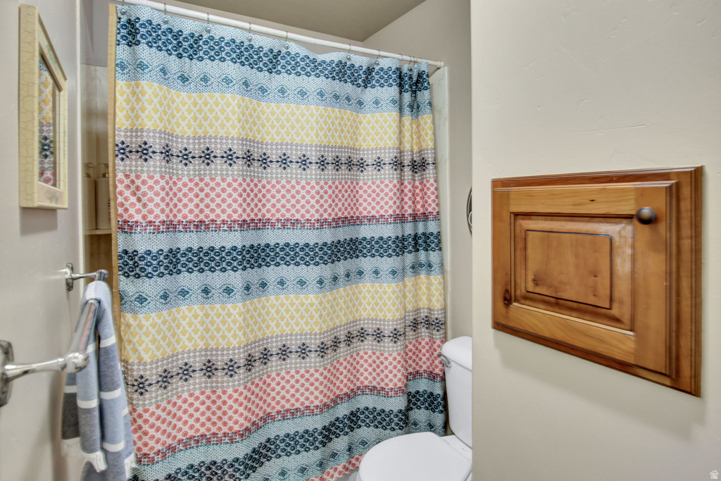 Built-in wall cabinetry with wood-finish door, polished chrome towel bar, and a toilet with a standard tank
