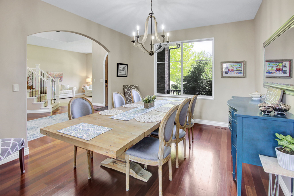 Dining area featuring rich wood-finish flooring, a large window, a chandelier, an arched doorway, and light-toned wall paint