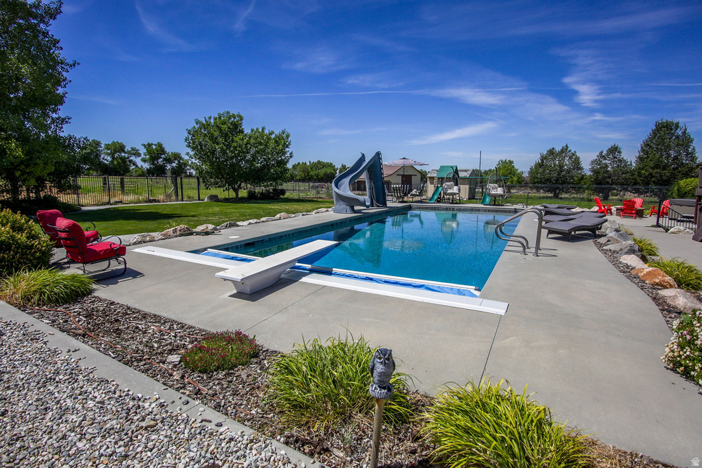 Expansive outdoor pool area featuring a diving board, water slide, concrete surround, and landscaped beds with gravel accents