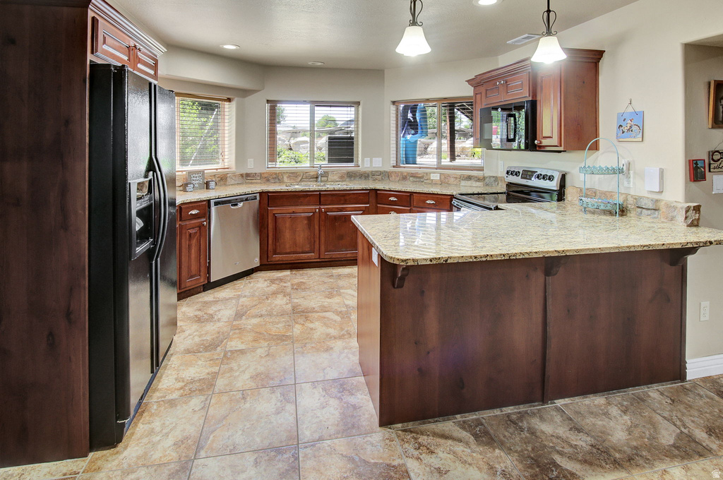 Kitchen featuring an eat-at island, stainless steel dishwasher, tile flooring, rich wood cabinetry, and a black refrigerator