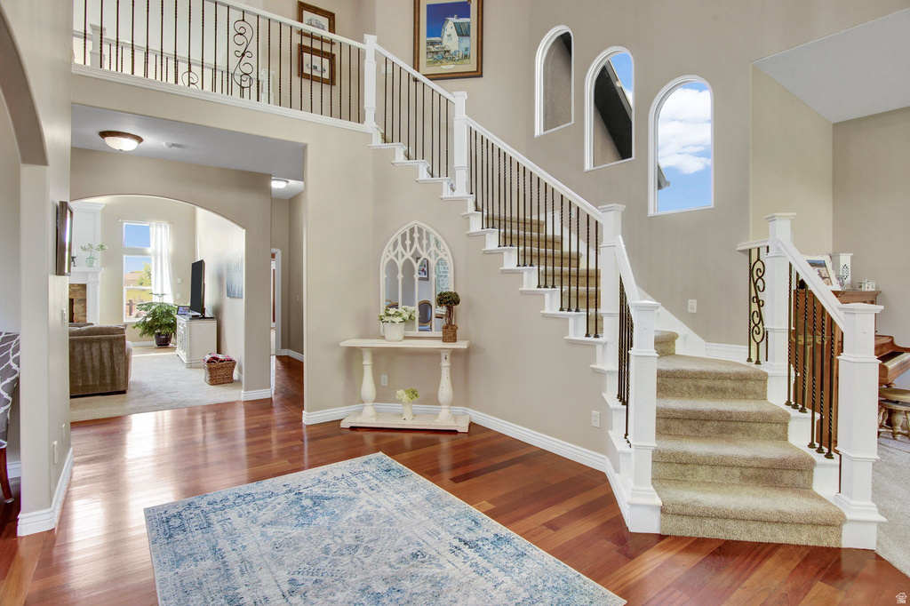 Entryway featuring a grand staircase with wrought iron balusters and carpeted treads, wood-finish flooring, arched doorways, and a second-story landing with matching balustrade