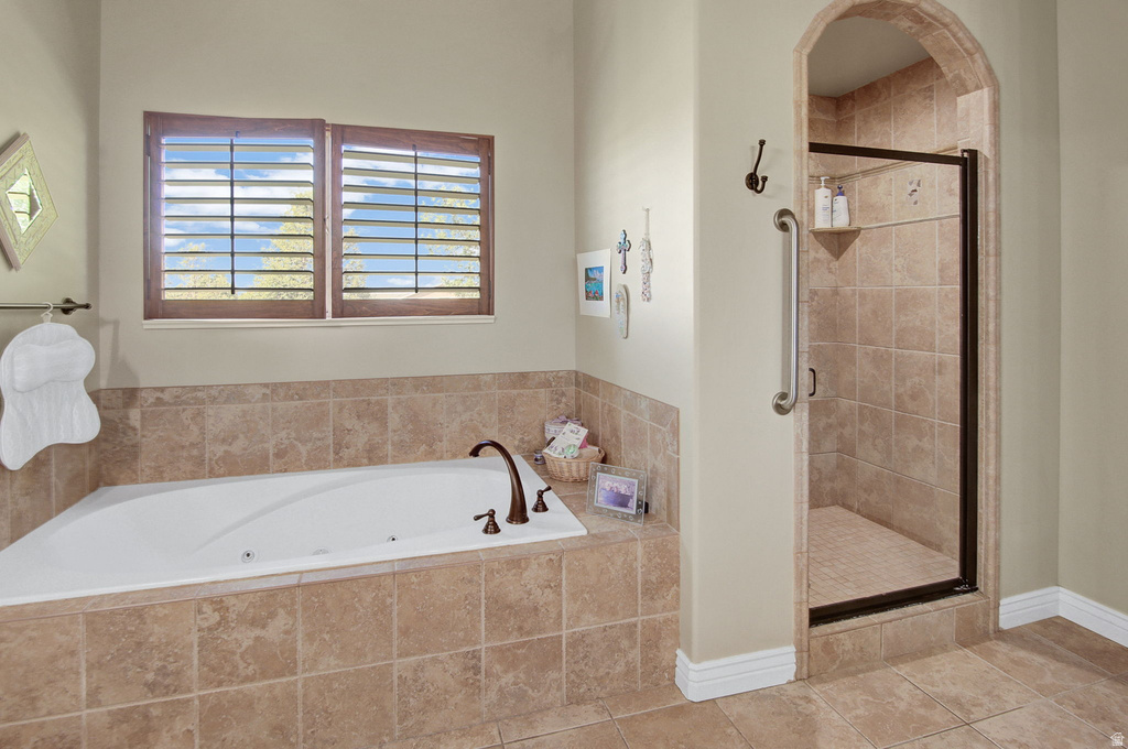 Soaking tub with bronze fixtures set into a tiled surround, complemented by a walk-in shower with an arched entry and glass door