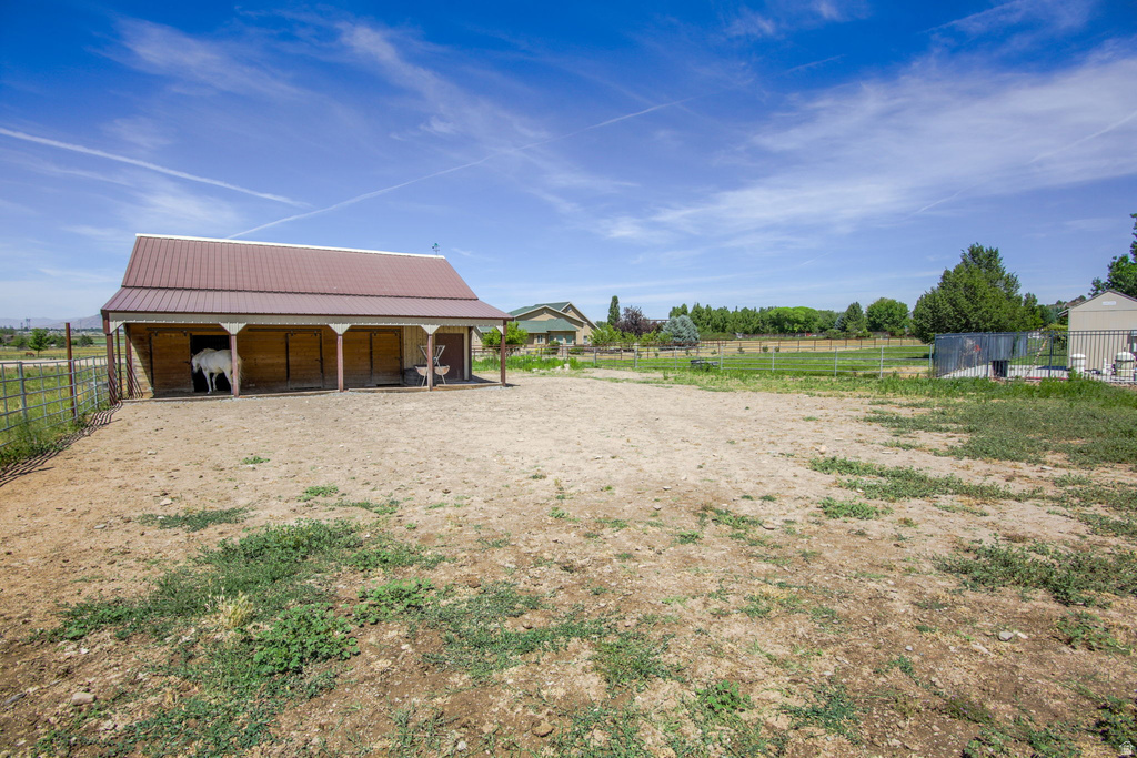 Barn structure featuring a brown metal roof, covered porch, multiple stalls, and a fenced enclosure