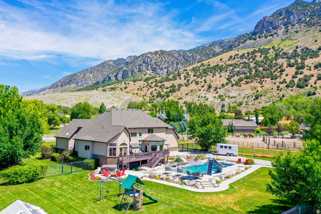Expansive backyard featuring a large in-ground swimming pool with slide, a spacious deck, mature trees, and a mountain backdrop