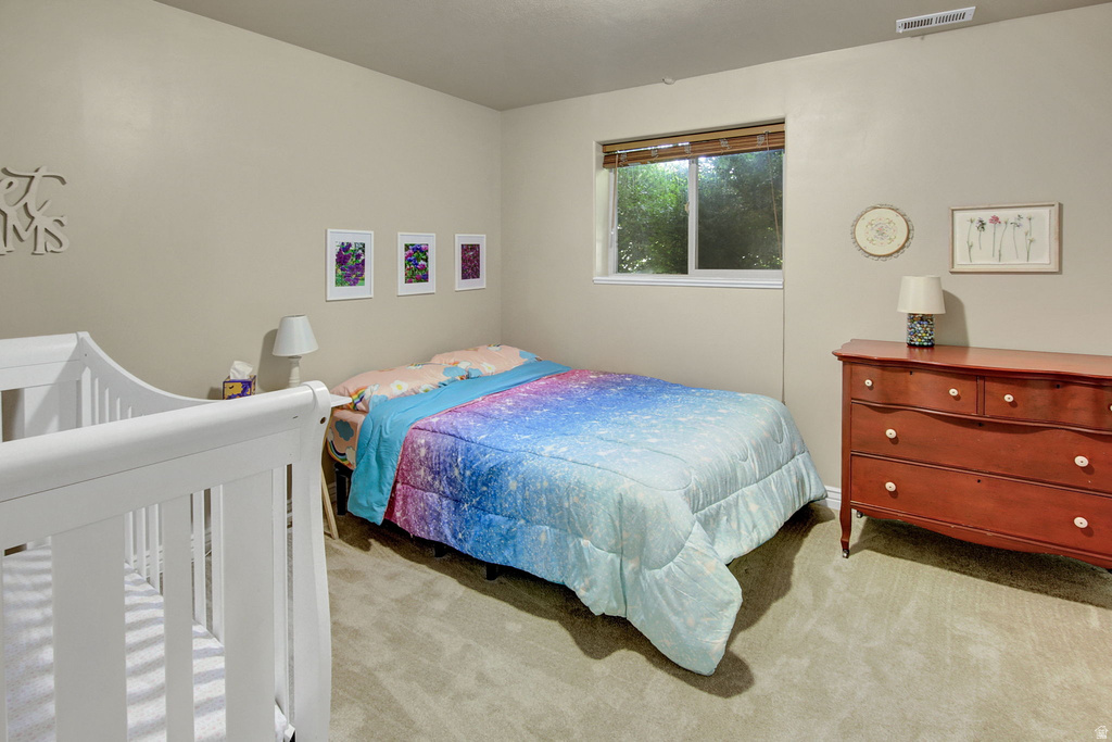 Carpeted room featuring a single window with blinds, light-colored walls, and a white crib
