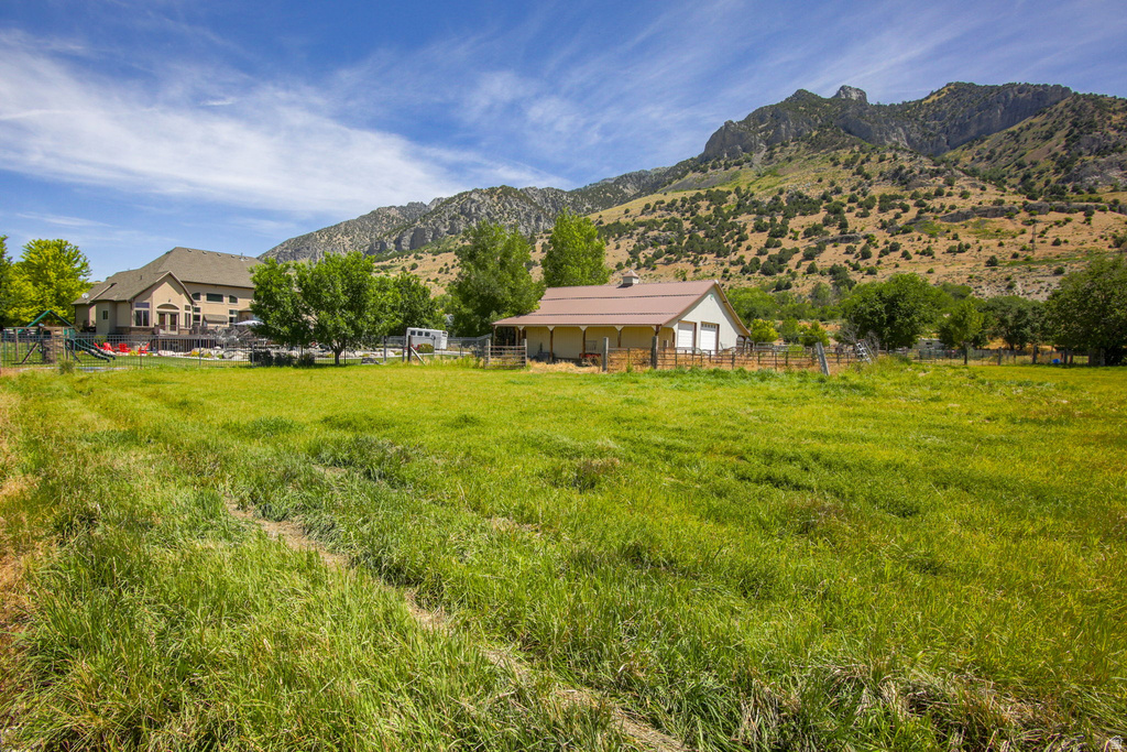Expansive green field bordering a detached structure with a brown roof and two garage doors, set against a backdrop of a mountainous landscape