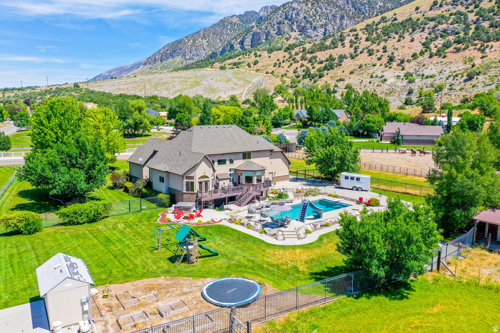 Expansive rear elevation featuring a multi-level deck, a swimming pool with a rock surround and slide, an outdoor play structure, and a fenced-in yard