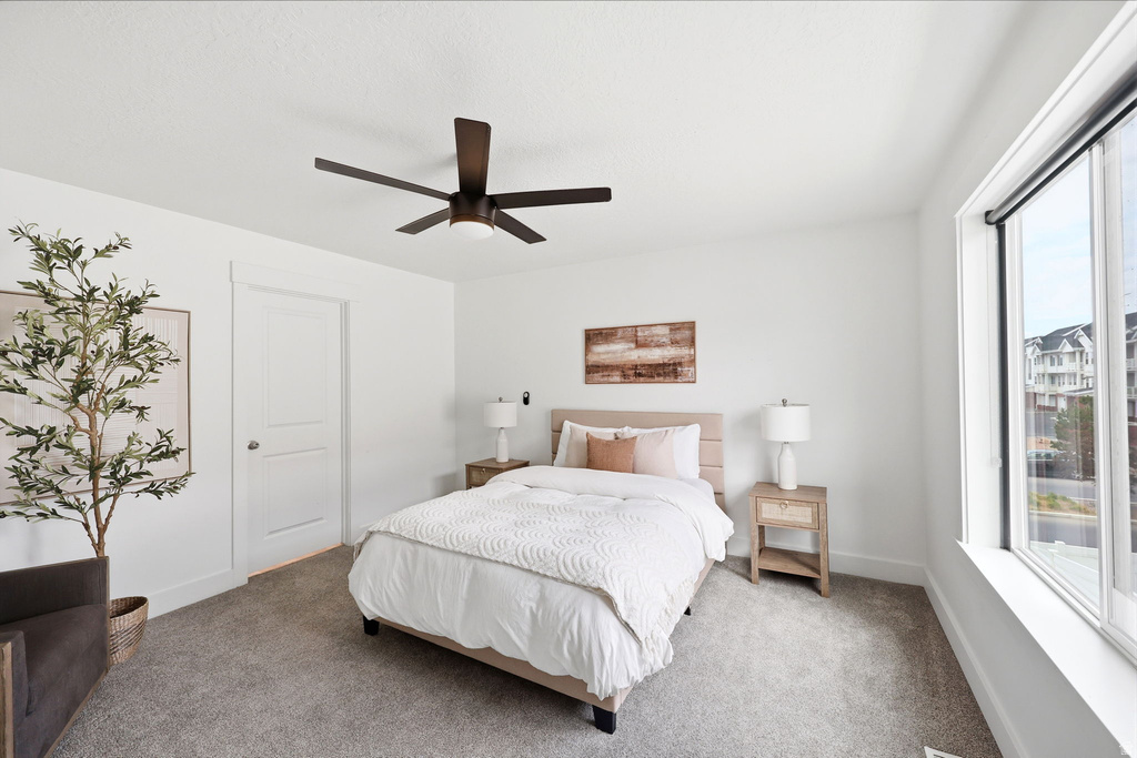 Bedroom featuring a contemporary ceiling fan, white trim, a solid door, and a large window with roller shades