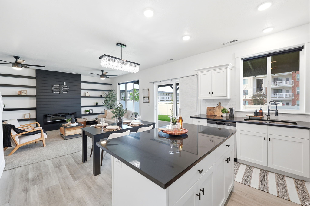 Open-concept kitchen and living area featuring white cabinetry, dark countertops, wood-finish flooring, a built-in fireplace, and a sliding glass door to the exterior