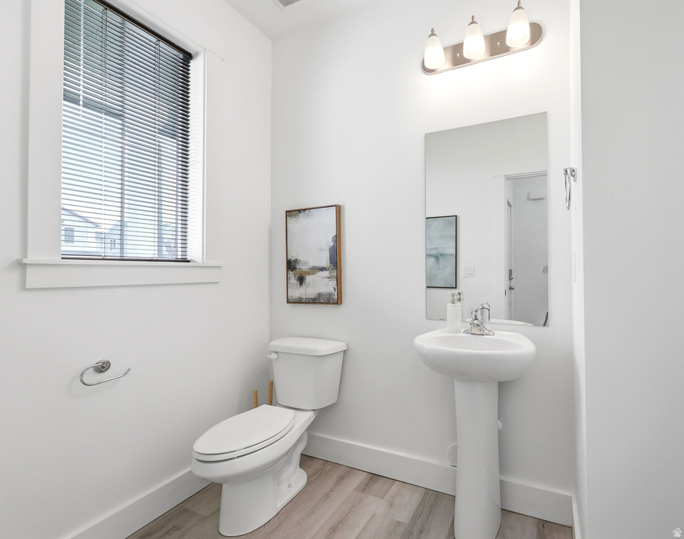 Bathroom featuring a pedestal sink, wall-mounted mirror, three-light vanity fixture, and wood-finish flooring