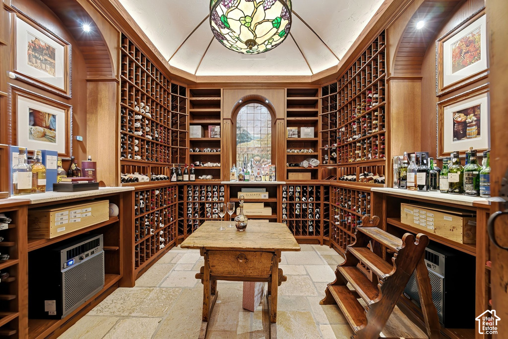 Dedicated wine cellar featuring extensive built-in wooden racking, stone tile flooring, a central wooden table, a stained-glass ceiling fixture, and a large arched window