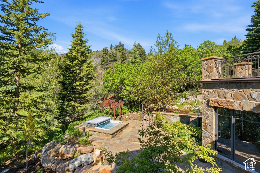 Outdoor patio featuring an integrated hot tub with stone surround, complemented by a natural stone retaining wall and extensive mature trees