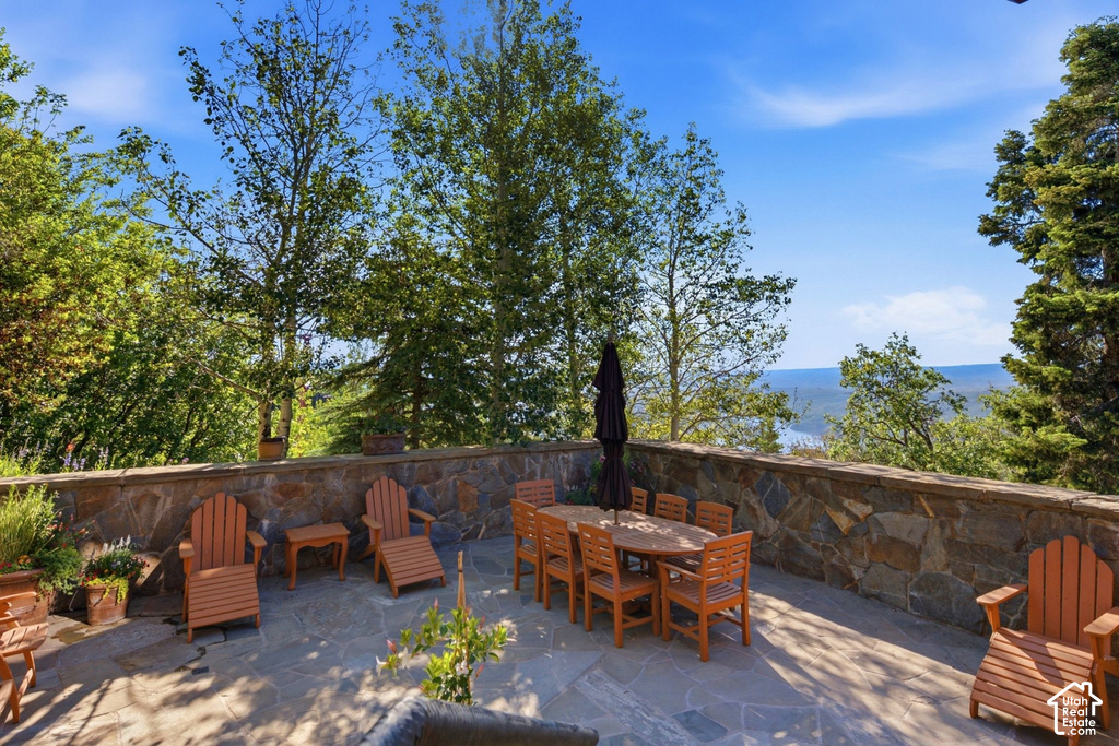 Expansive stone patio featuring a natural stone wall, mature trees, and a distant water backdrop