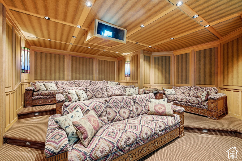 Dedicated media room featuring tiered seating, wood-paneled walls, recessed ceiling lighting, and a built-in projector with screen